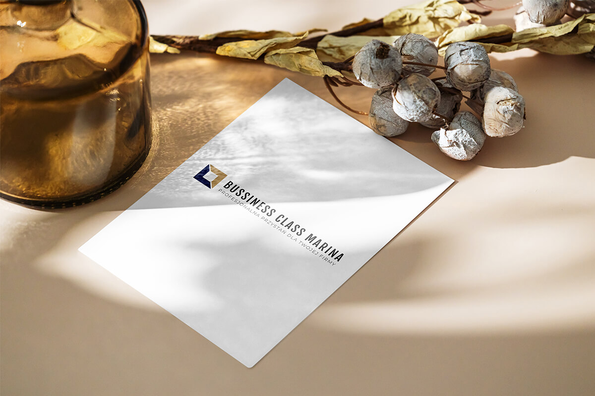 logo Business Class Marina na kartce papieru, lezącej na stole. Wokół dekoracje w kolorach brązu